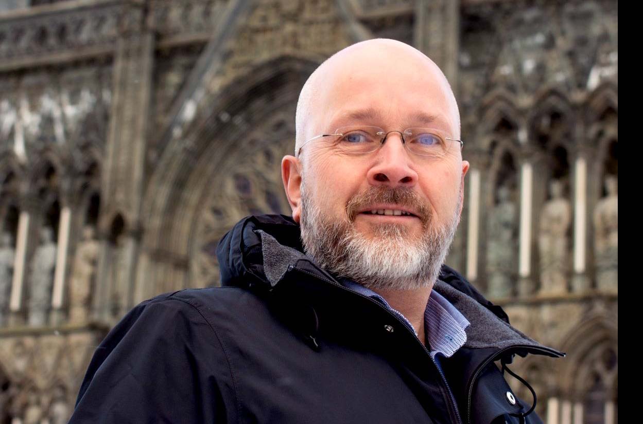 Skallet mann med mørk jakke og nesten usynlige briller foran Nidarosdomen